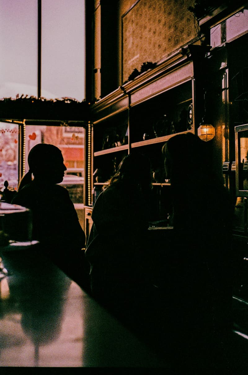 Three people in silhouette at a café counter, lit by a warm hanging lamp