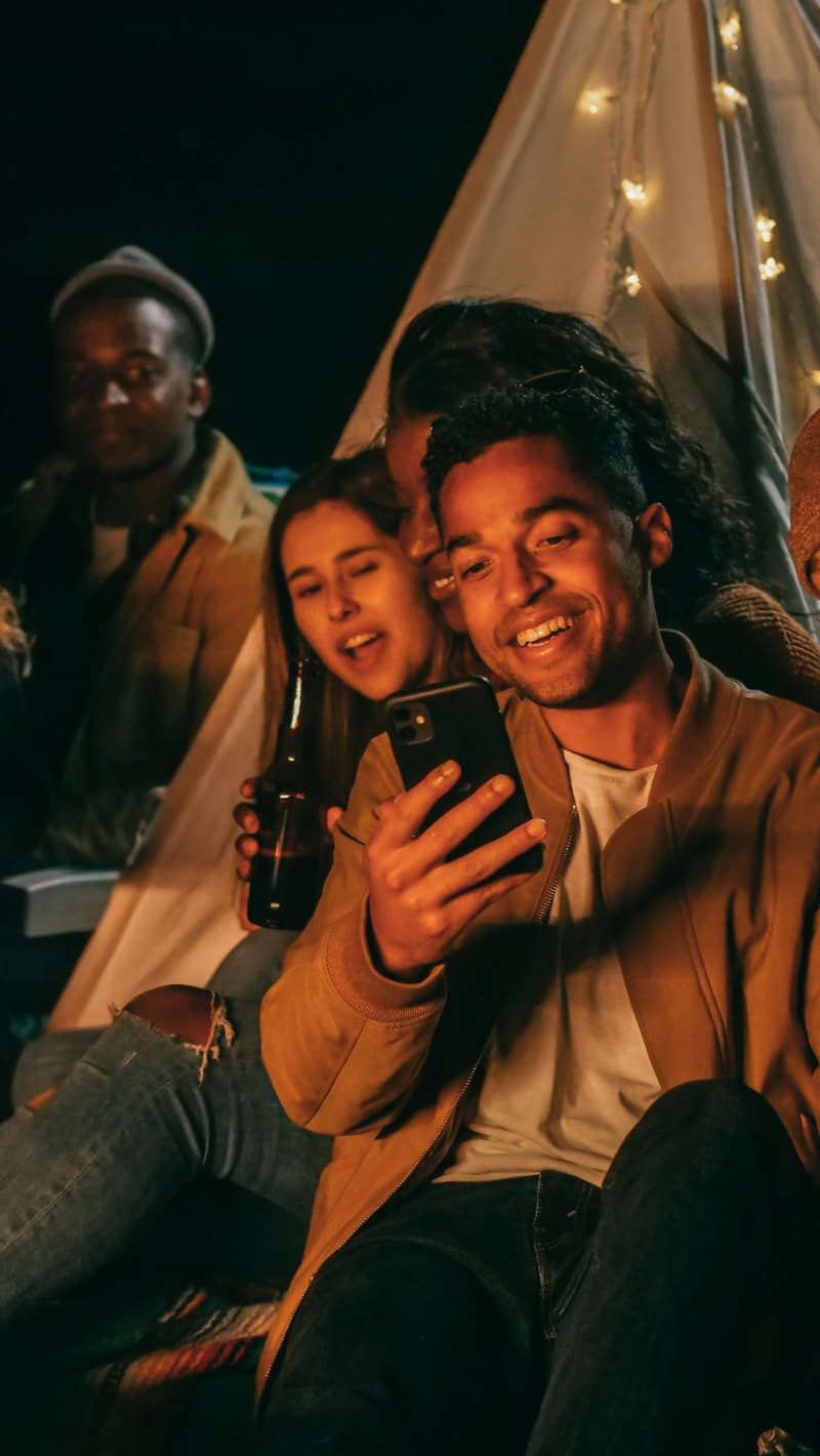 Friends laughing together outdoors at night under warm string lights